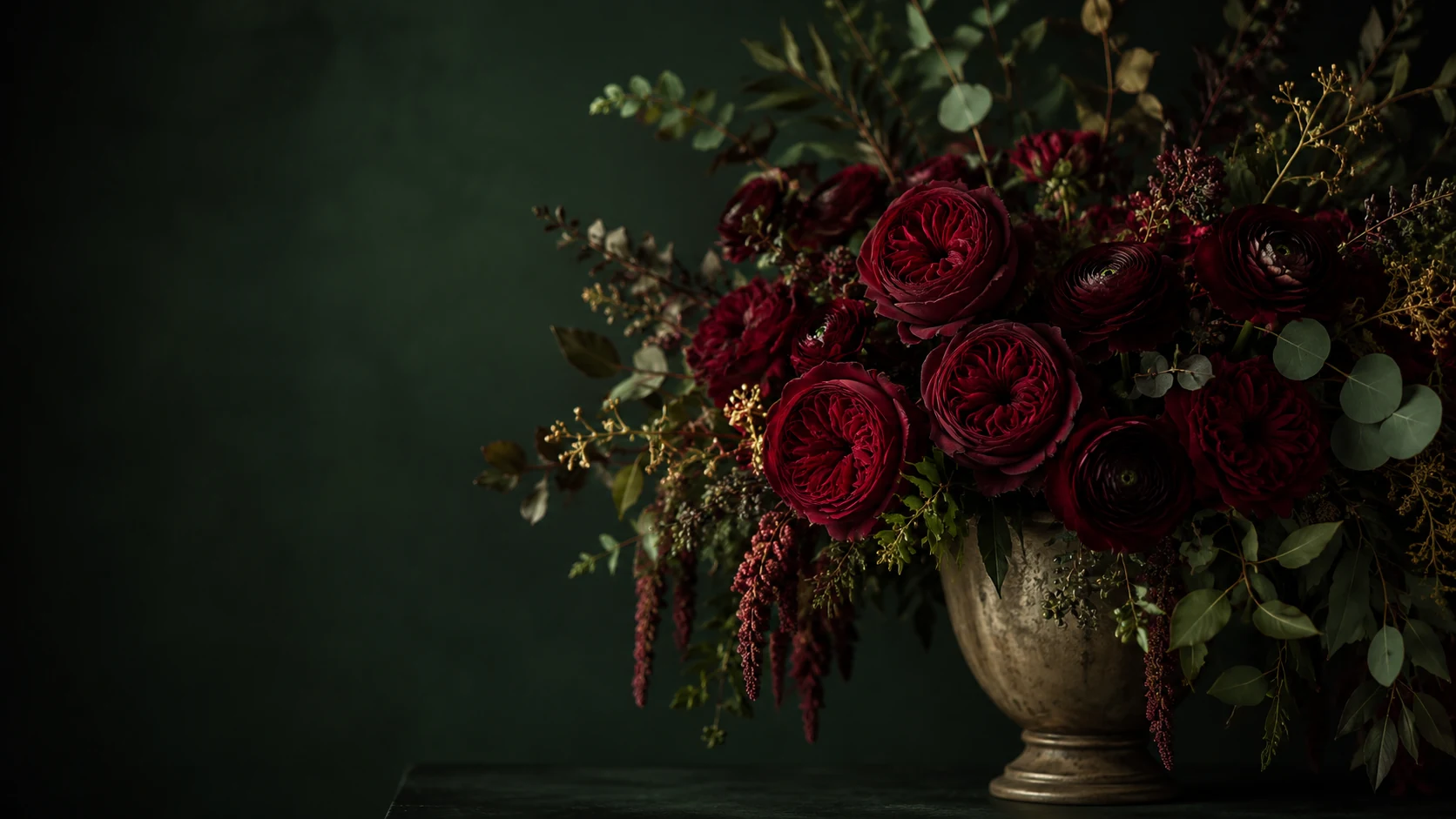Sculptural burgundy rose arrangement in an antique gold vessel